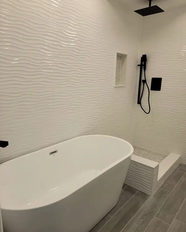 Freestanding tub beside a textured white feature wall with a black shower set