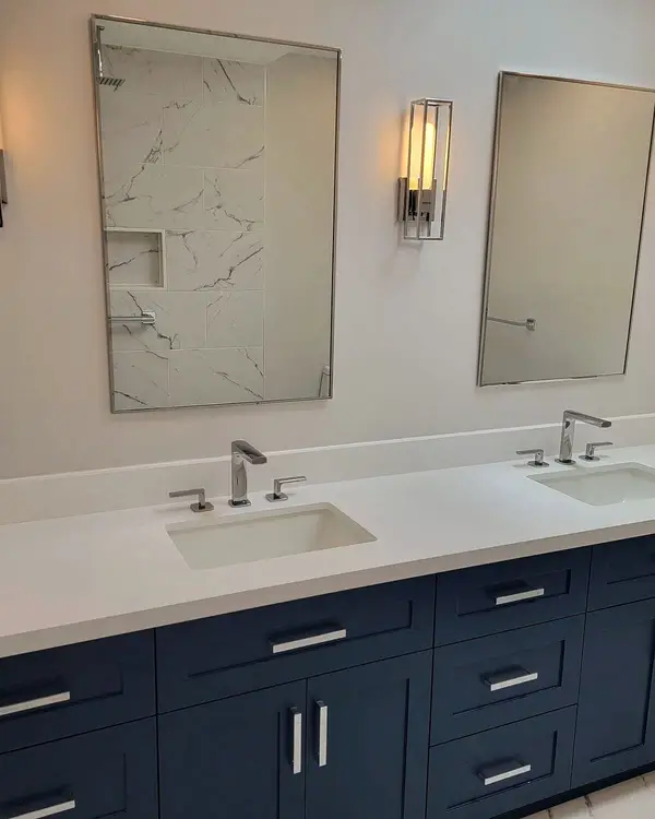 Navy double vanity with brass sconces in a renovated bathroom