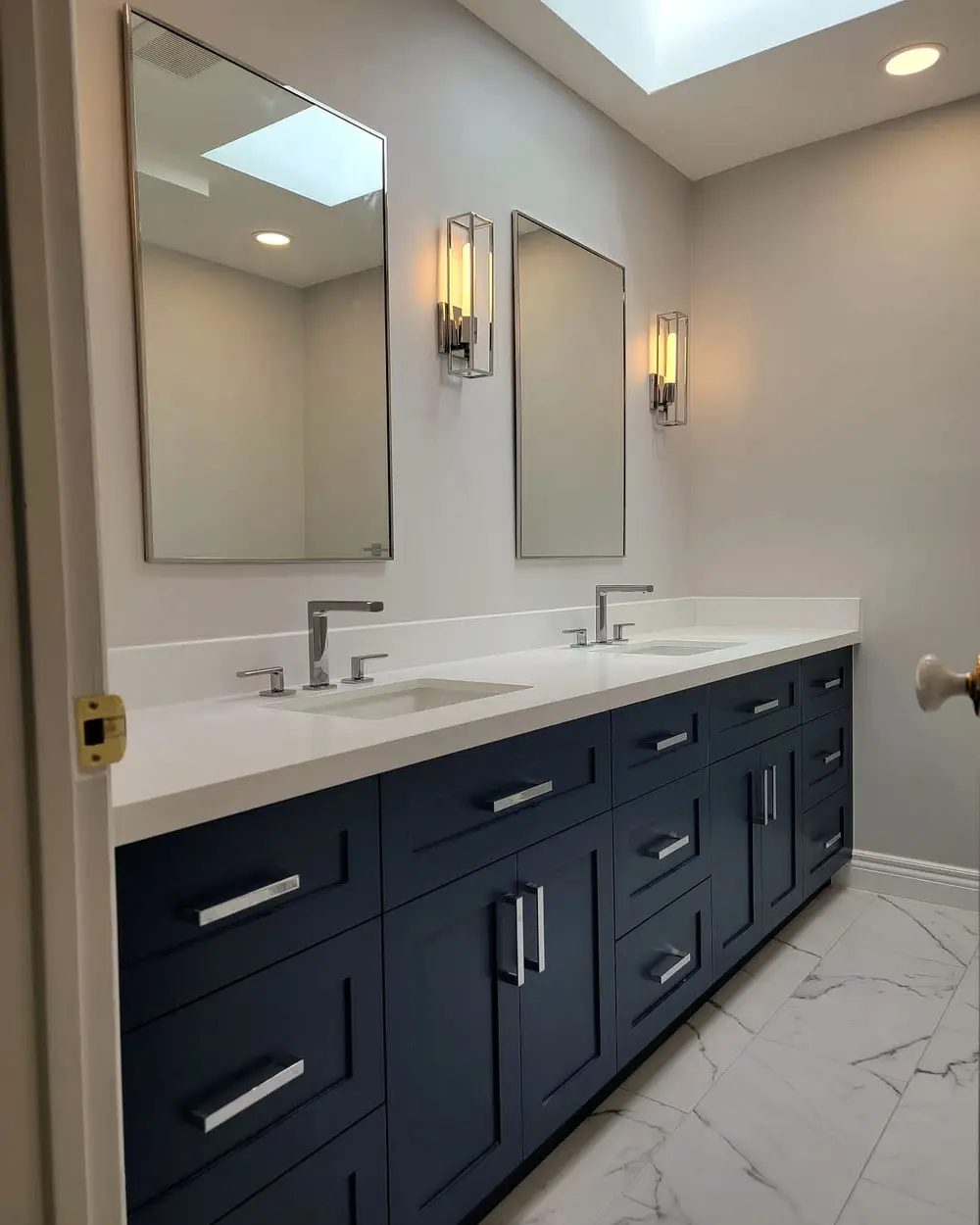 Navy double vanity with brass sconces and a skylight