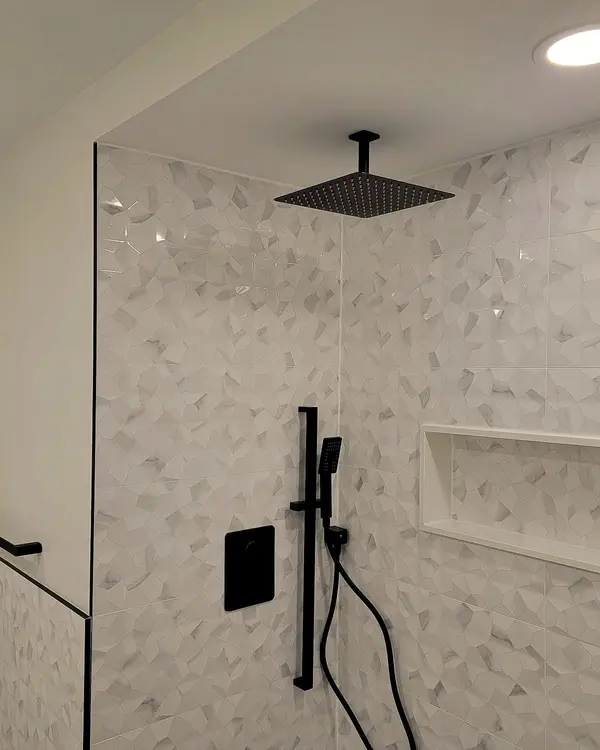 Glass shower with a textured white tile wall and a black rain head