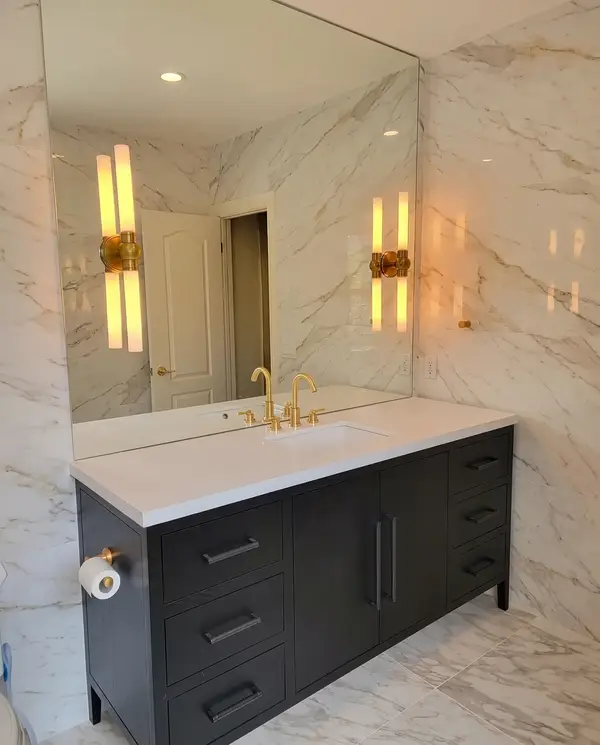 Black vanity with brass sconces against marble-look slab walls