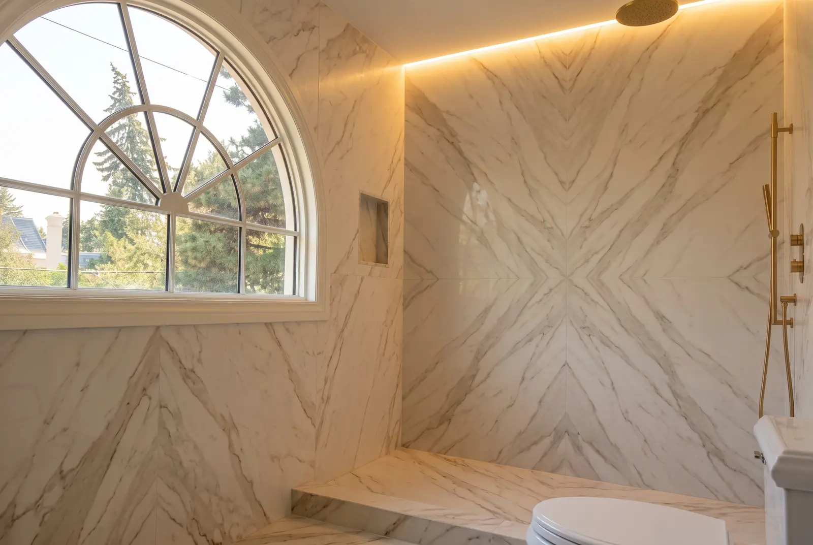 Curbless shower under an arched window, lined in bookmatched marble-look slabs