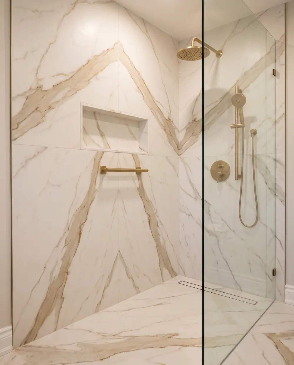 Walk-in shower in bookmatched marble-look slabs with brass fixtures and a slab-lined niche