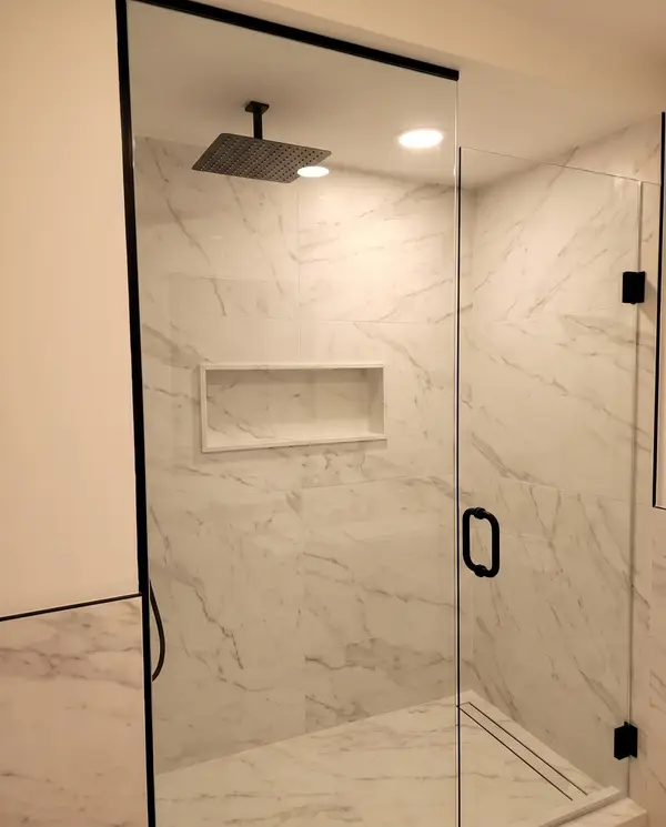 Frameless glass shower in large marble-look slabs with a linear drain