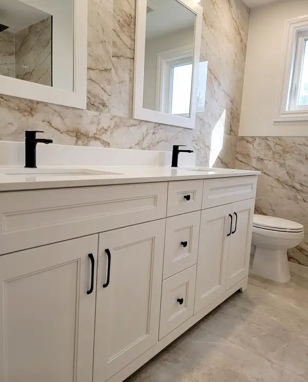 White shaker double vanity with black faucets and a marble slab feature wall