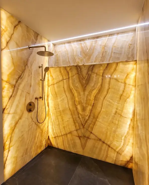 Backlit onyx-look slab shower with brushed brass fixtures and a charcoal floor